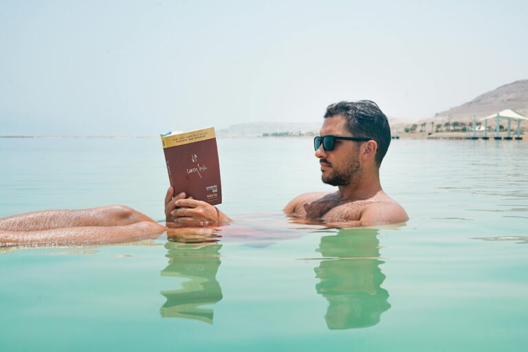 Relaxing man reading a book while floating on the Dead Sea under bright sunlight.